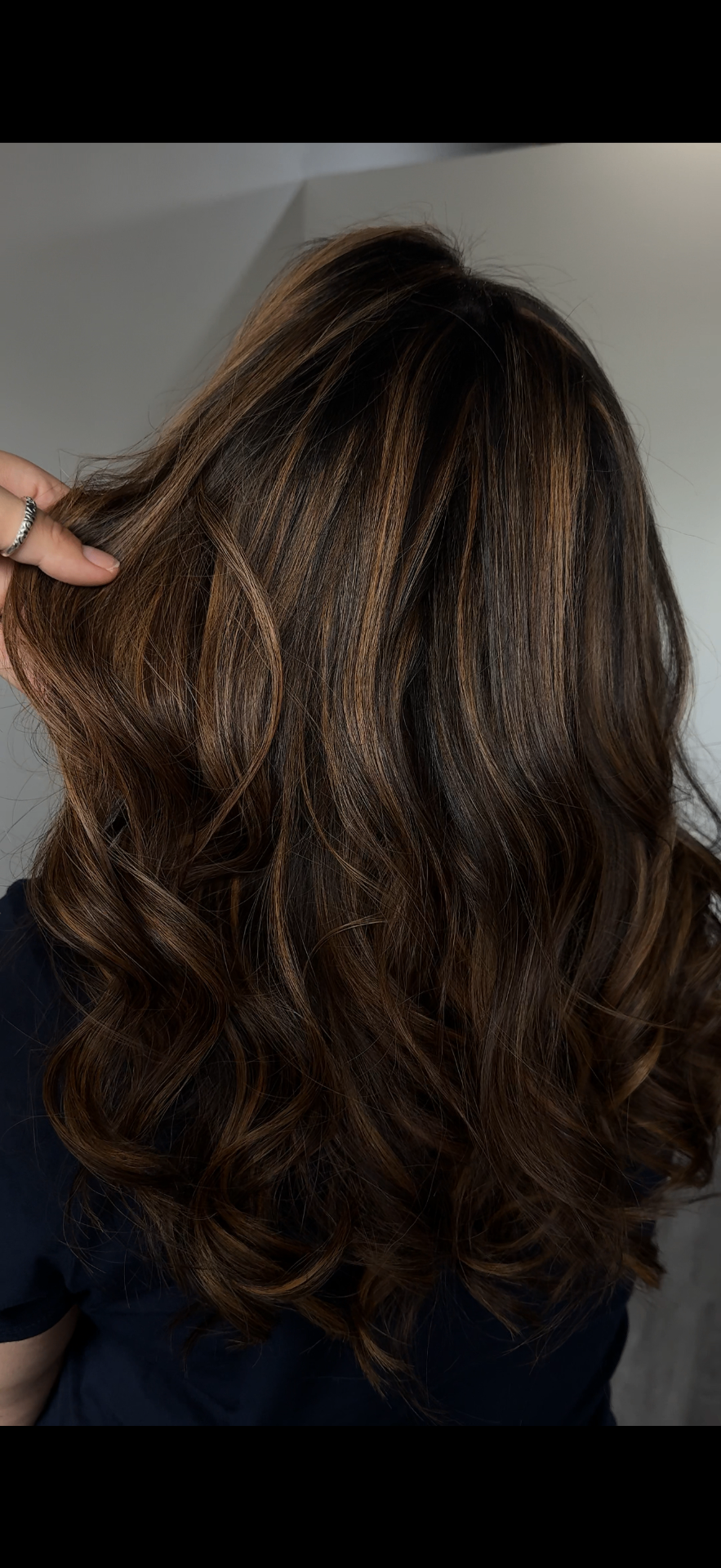 Rich brunette with warm caramel balayage highlights, styled in loose waves